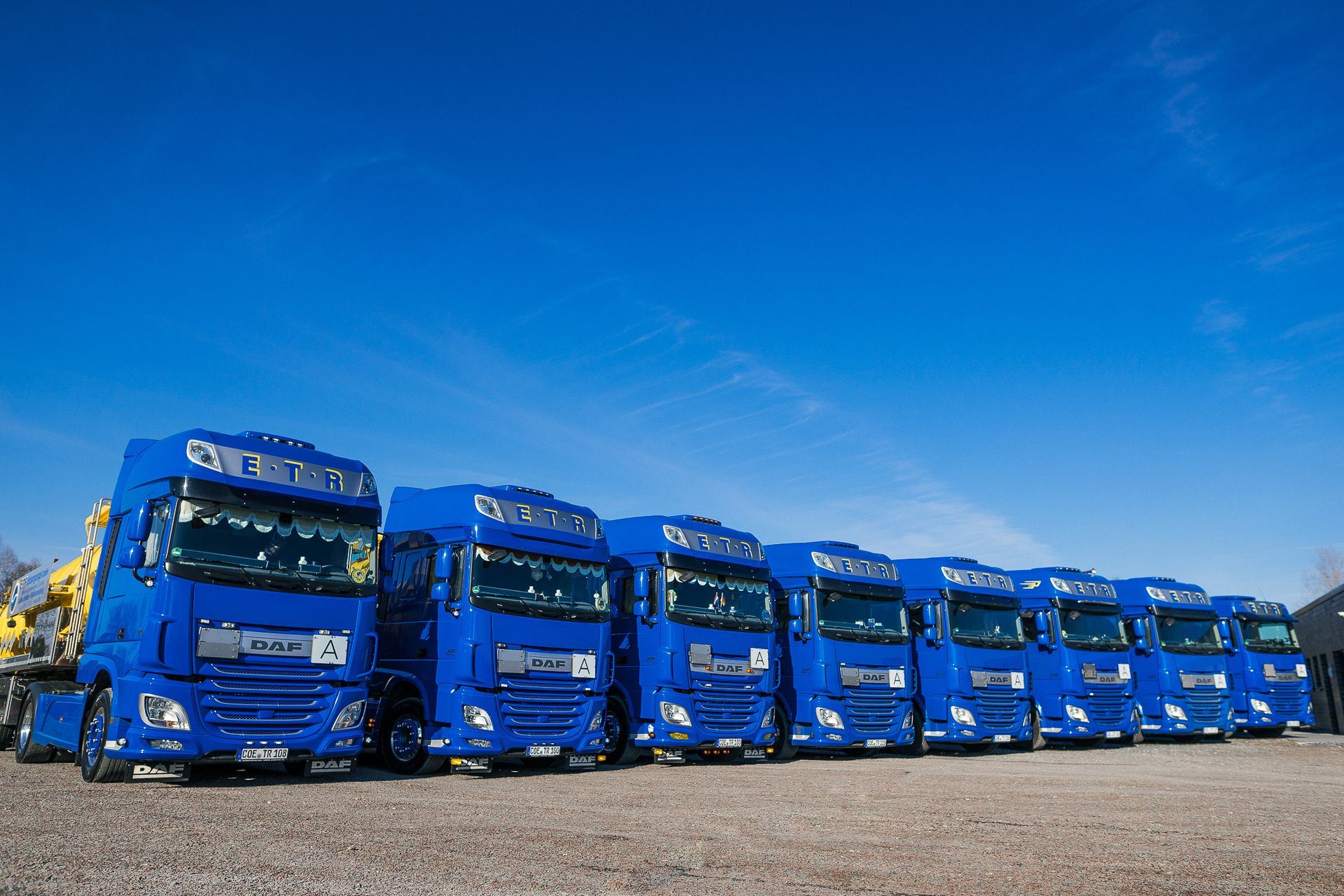Reihe blauer DAF Lkw mit Aufliegern, aufgereiht auf einem Parkplatz unter blauem Himmel, eingesetzt für Schwerlast- und Transportlogistik